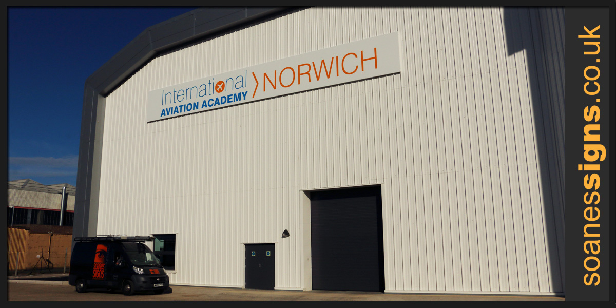 Installation, hangar sign in six sections fabricated from white folded pans with aluminium rail support and vinyl graphics applied, installed for International Aviation Academy Norwich